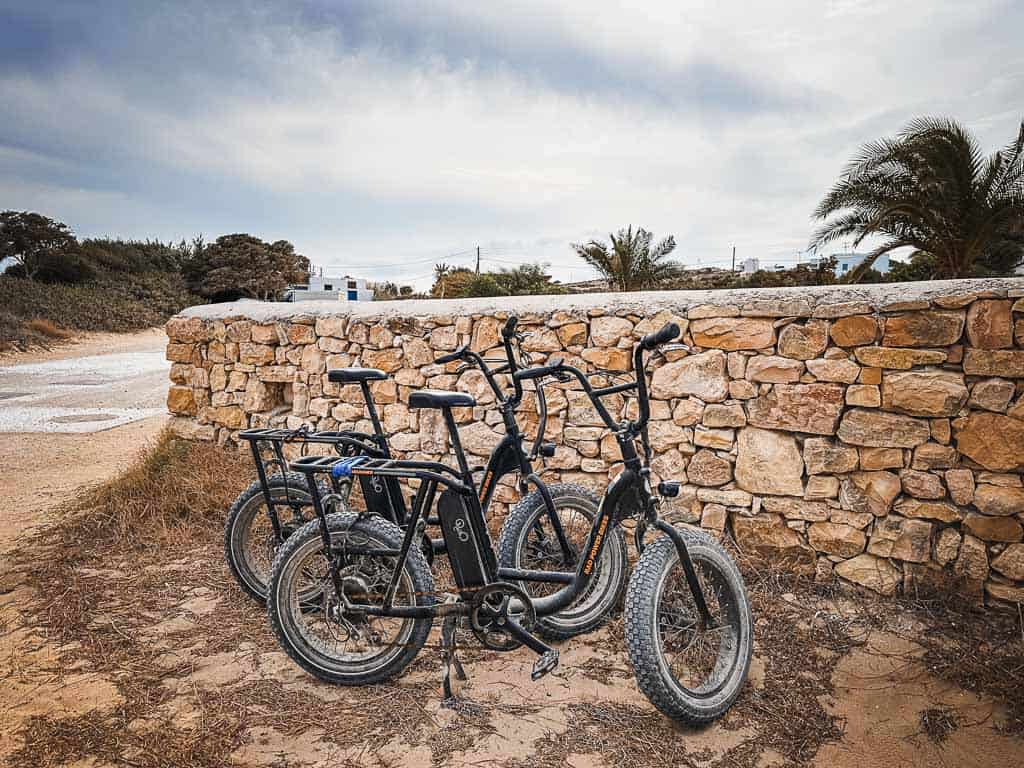 3 black E-bike rentals in Koufonisia Greece lined up against a stone wall