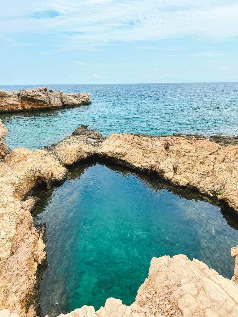 A turquoise natural pool formed into the cliffside overlooking the Aegean Sea in Koufonisia Greece